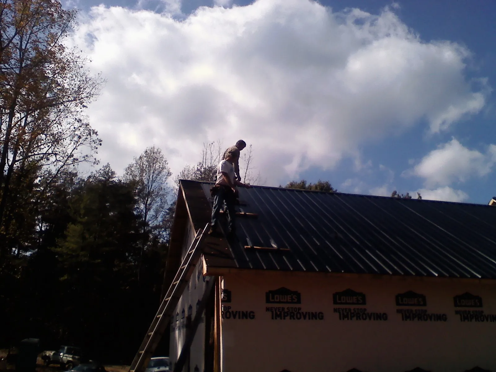 Roofer fastening dark metal panels high against a cloudy sky, from a Roof Inspection job in Lawton