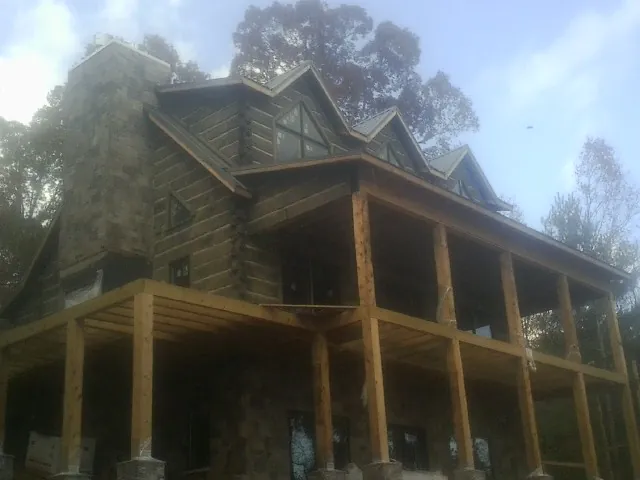 Stone chimney and dormers on a large log home with a timber porch in Lawton