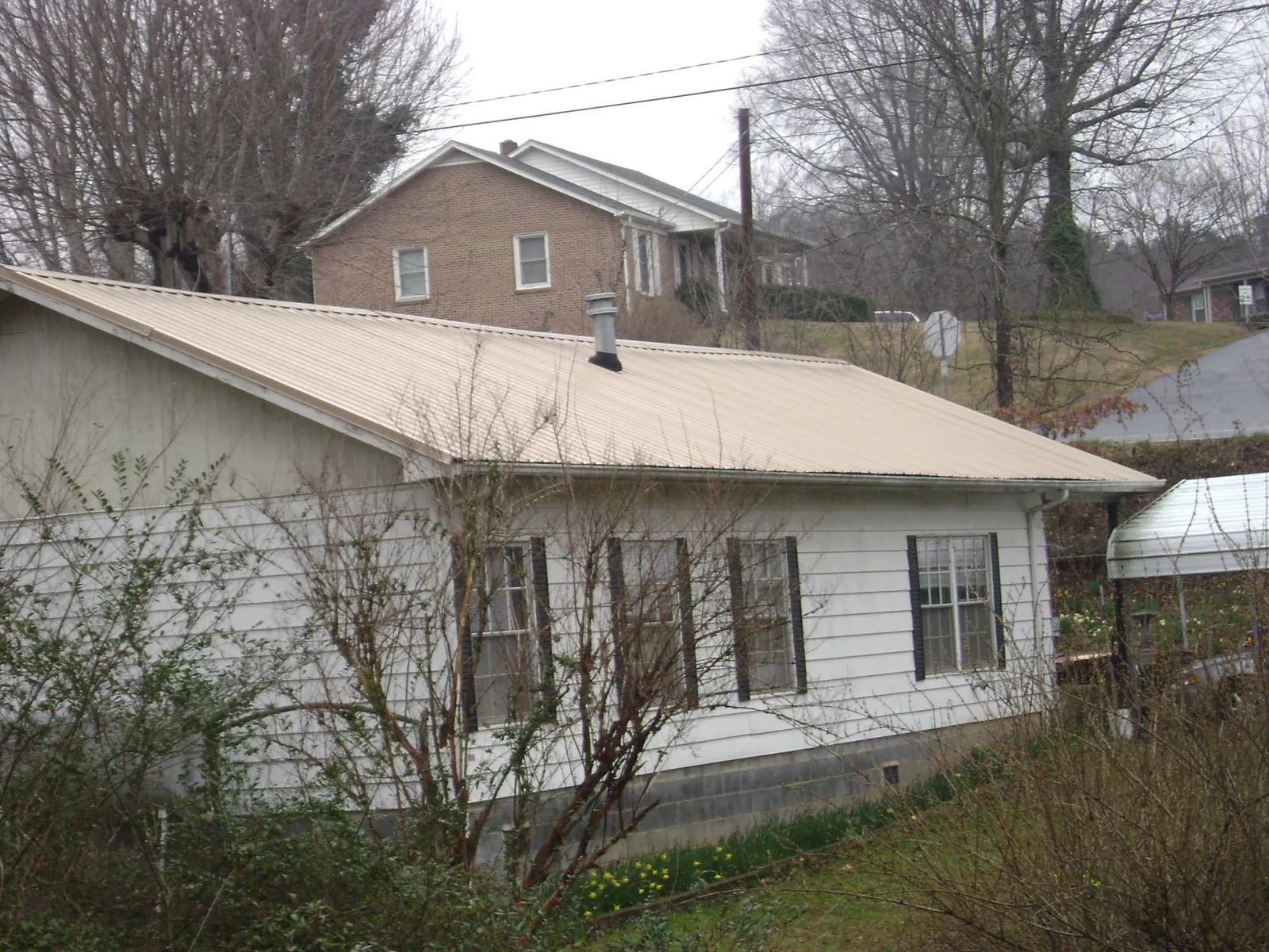 Tan metal roof on a white sided house set into a hillside — Commercial Roofing by Roofing Brothers in Lawton